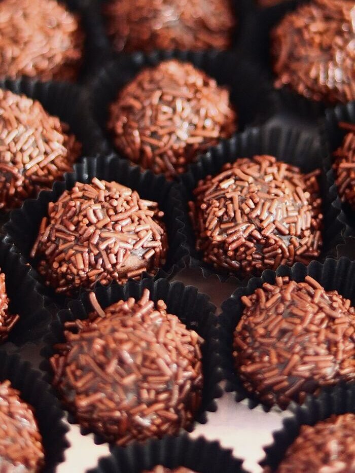 Close-up of chocolate brigadeiros with sprinkles in black cup liners. Sweet indulgence captured.